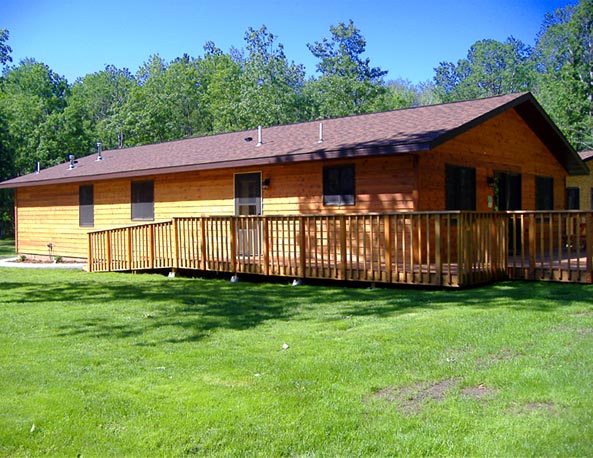 Outside View of Cabin #18 with large deck, BBQ grill and picnic table.  The deck faces North; parking is at the south of this cabin.  The Ramp shown here leads to the kitchen entry door and the spacious deck.